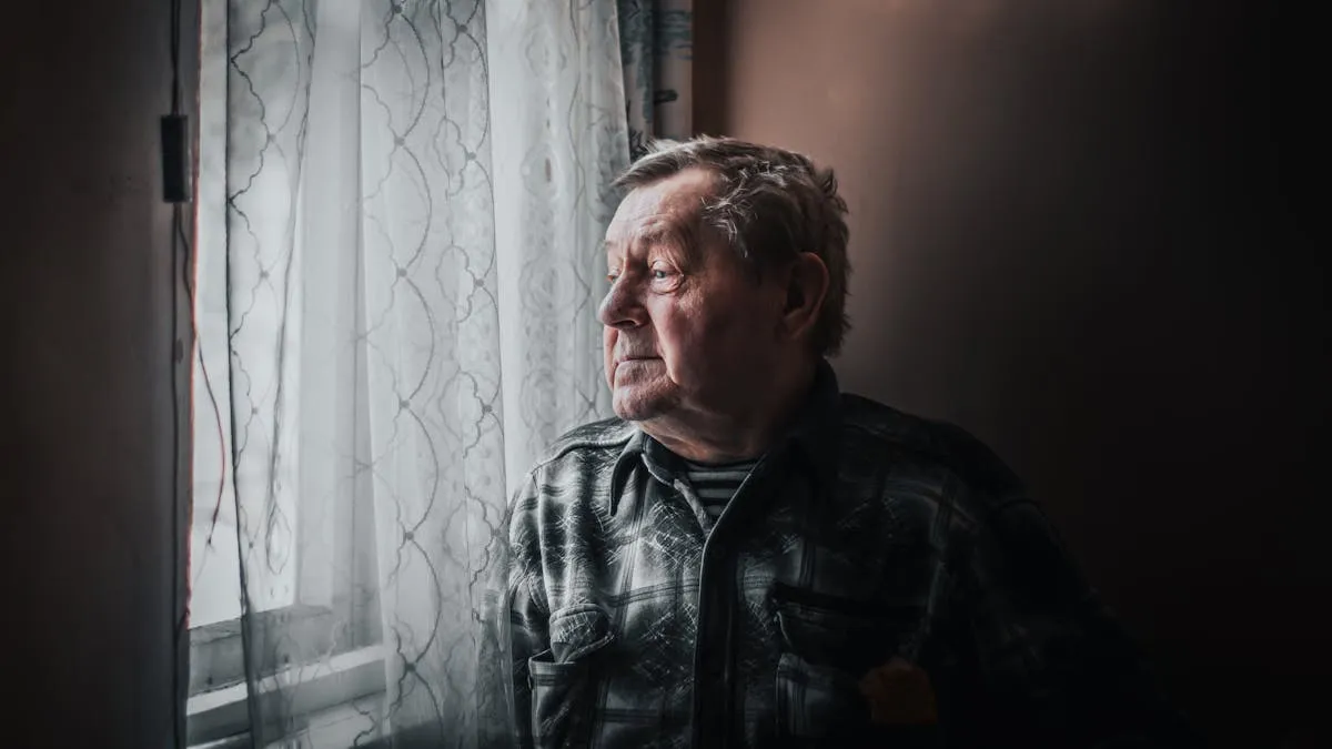 An elderly man looking thoughtfully out a window, representing the confusion and contemplation that can accompany sundowning in seniors
