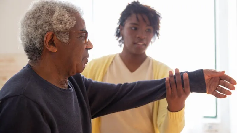 A caregiver gently helping an elderly man with exercises in a warm home setting during evening hours