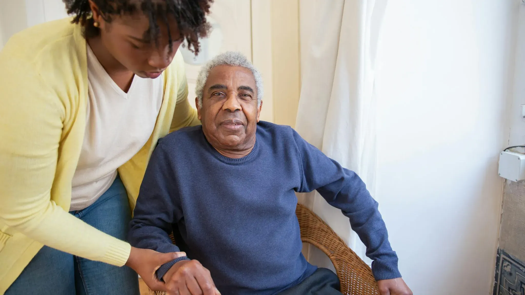 Elderly person resting in a comfortable chair during daytime while a family member looks on with concern